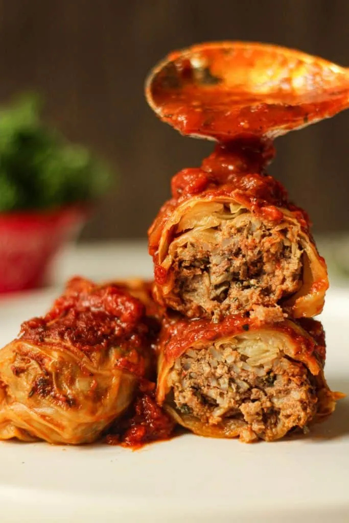 stuffed cabbage rolls cut in half being topped with a spoonful of extra sauce