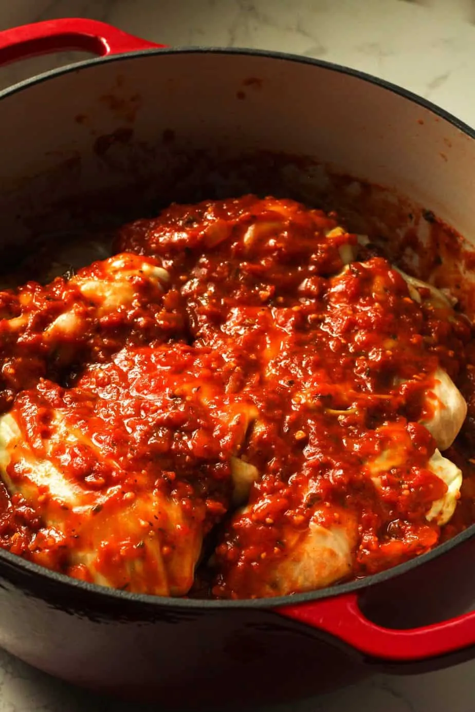 prepared stuffed cabbage rolls layered in a Dutch oven topped with sauce