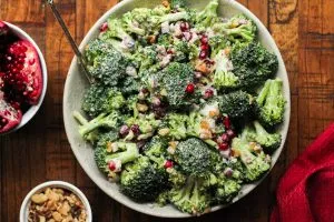 Broccoli pomegranate salad in a white bowl on a wooden surface.