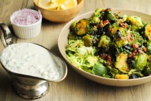 Close up of roasted brussel sprouts salad and blue cheese in separate dishes on a wooden surface.